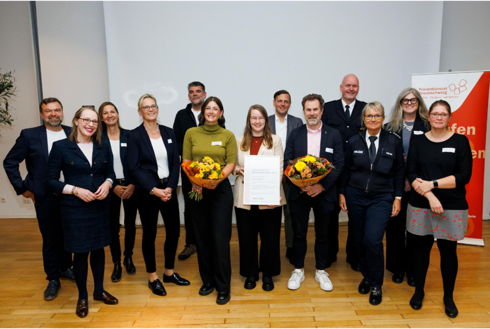Gruppe von Erwachsenen mittig zwei Geehrte mit Urkunde und Blumen